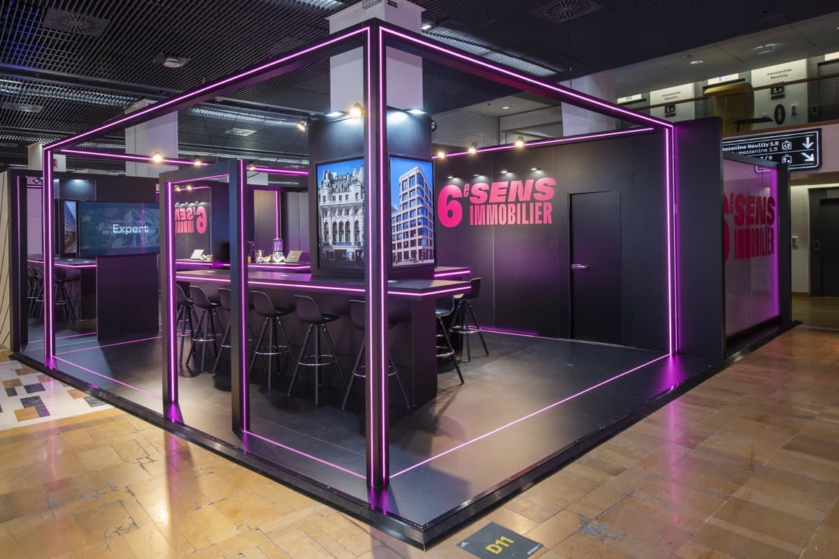 Stand 6ème Sens Immobilier au SIMI, structure noire à liséré néon rose et bar d'accueil, conçu et réalisé par The Good Experience