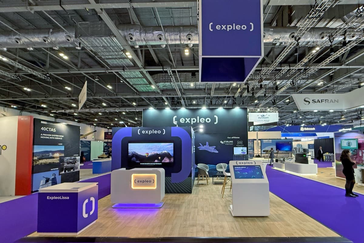 Stand Expleo à DSEI, structure arquée violette et blanche avec écran immersif et bornes interactives, conçu et réalisé par The Good Experience