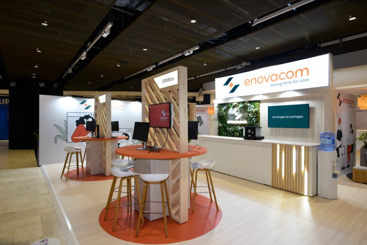 Stand Enovacom aux Journées Francophones de Radiologie, bois clair et mur végétal avec postes de démonstration, conçu et réalisé par The Good Experience